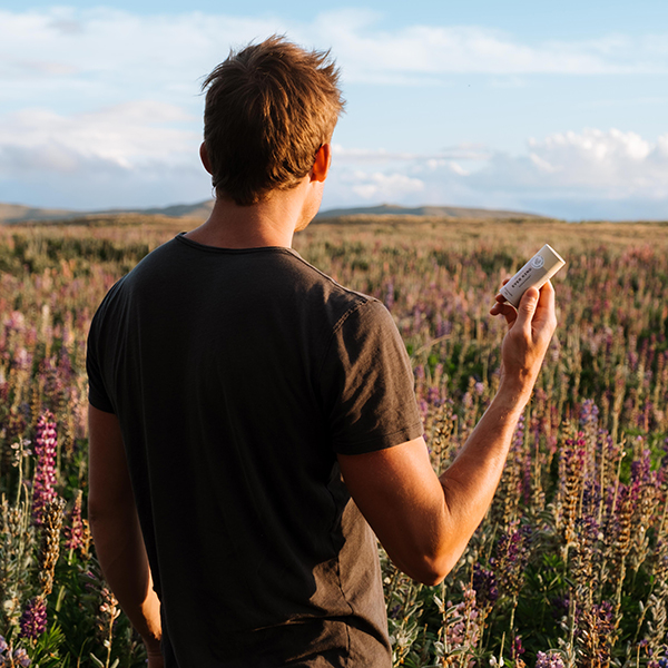 Man in New Zealand lupin field holding Everkind natural deodorant for men.